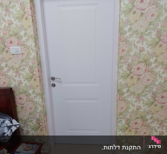 דלת לבנה עם ידית מתכת על רקע טפט פרחוני